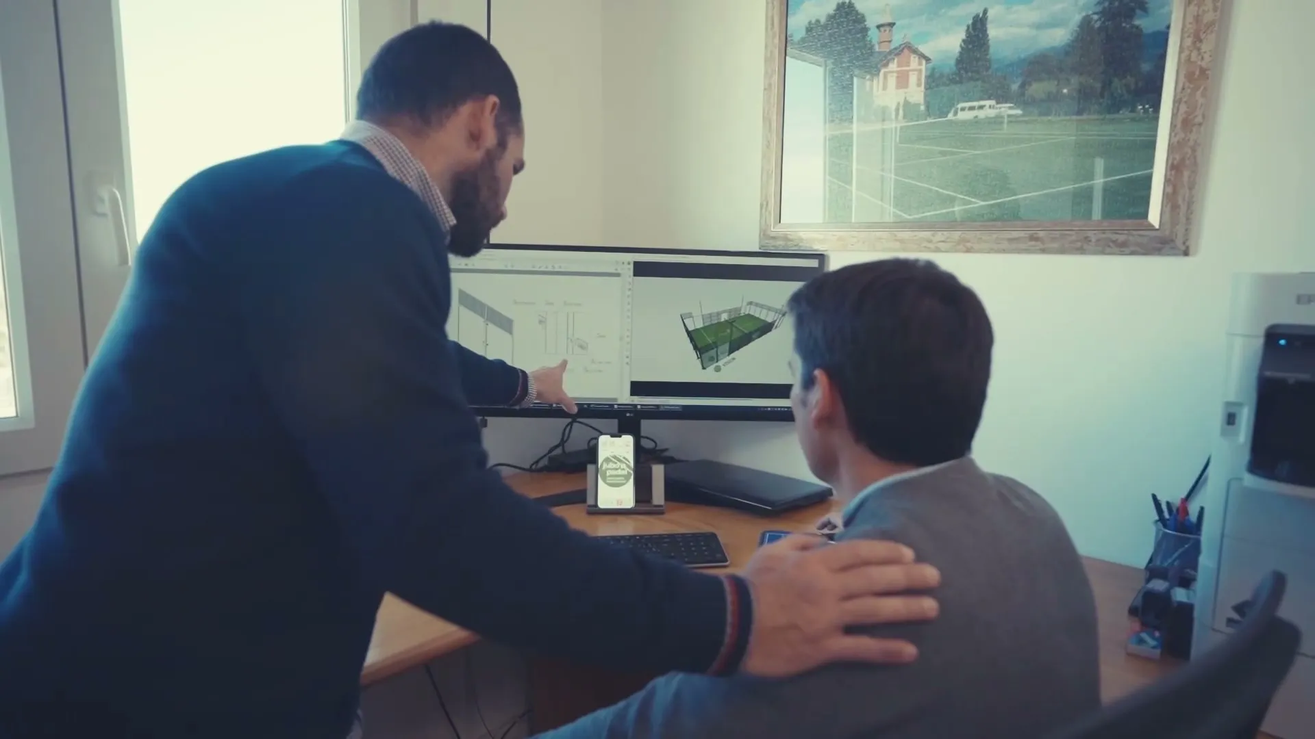 Zwei Personen vor einem Bildschirm mit technischer Zeichnung und 3D-Modell eines Padelplatzes